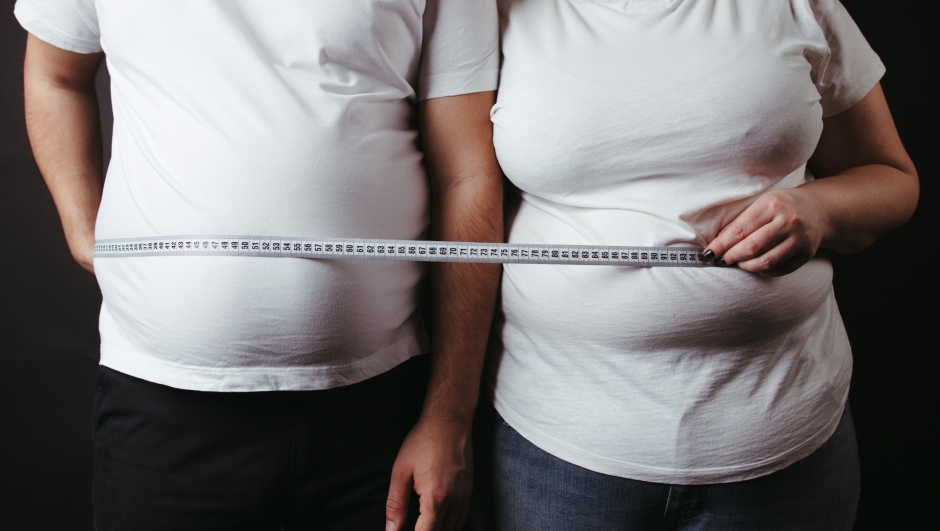 Overweight couple standing together wrapped with measure tape. Dieting, family weight loss and health care