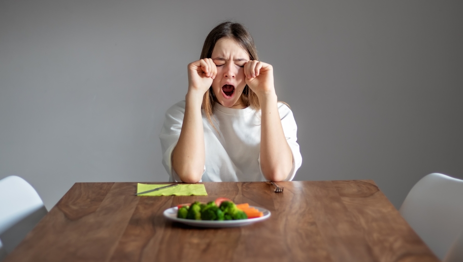 No vegan diet concept. Teenager girl yawning sitting at the table doesn.t want to eat healthy food -  broccoli and other vegetables. Food waste. Copy space. Late riser.