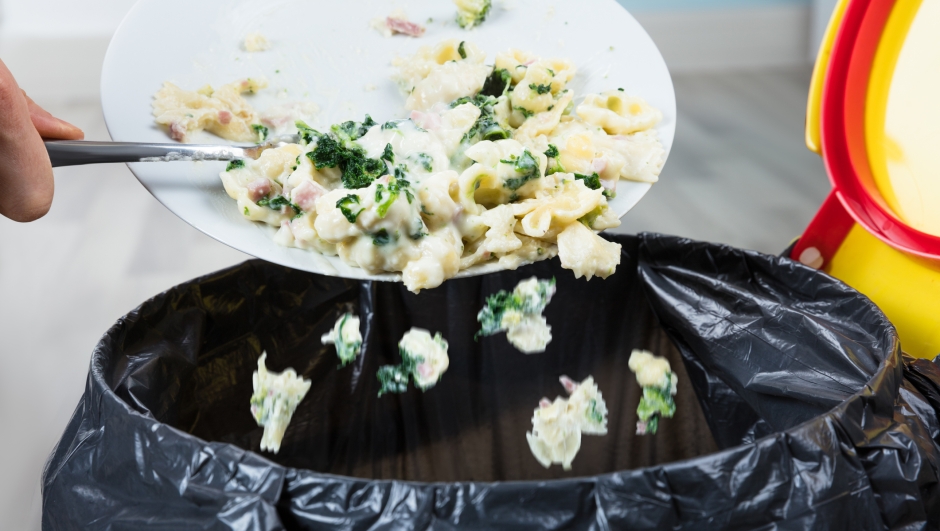 Close-up Of A Person Throwing The Leftover Pasta Into The Trash Bin