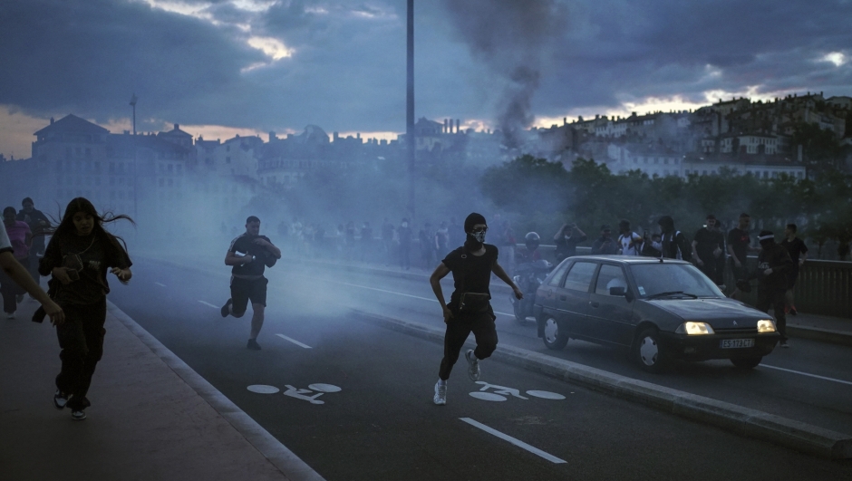 People run away during clashes with police in the center of Lyon, central France, Friday, June 30, 2023. French President Emmanuel Macron urged parents Friday to keep teenagers at home and proposed restrictions on social media to quell rioting spreading across France over the fatal police shooting of a 17-year-old driver. Writing on wall reads in French "Justice for Nahel" (AP Photo/Laurent Cipriani)