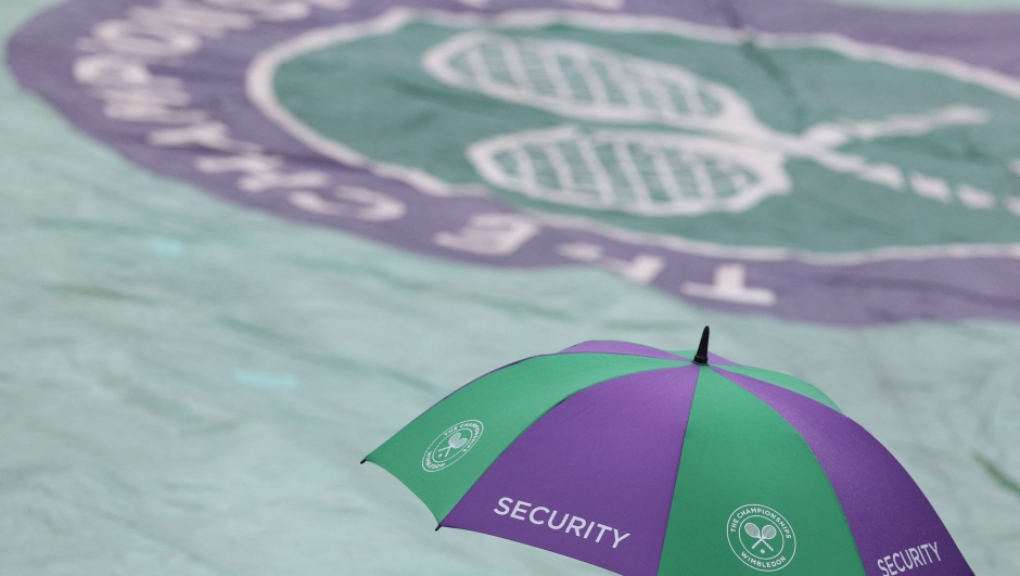 A security member holds an umbrella next to a covered court as the rain starts to fall on the first day of the 2023 Wimbledon Championships at The All England Tennis Club in Wimbledon, southwest London, on July 3, 2023. (Photo by Adrian DENNIS / AFP) / RESTRICTED TO EDITORIAL USE