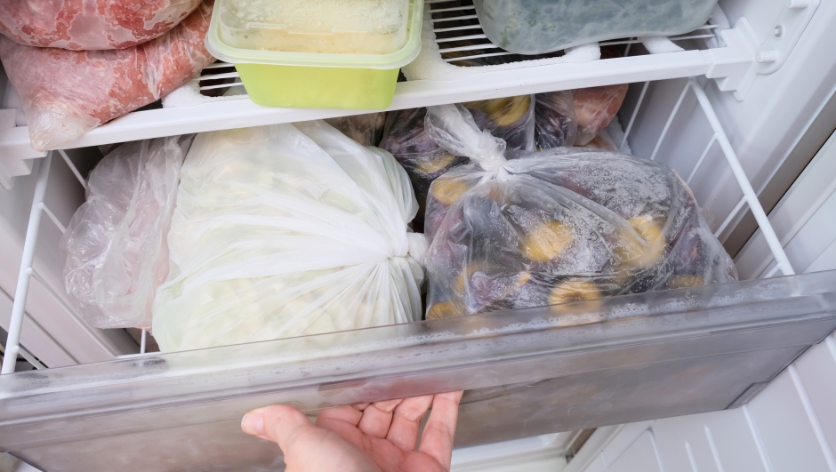 A hand opening a drawer of a freezer with frozen foods, long-term food storage and inventory at home.
