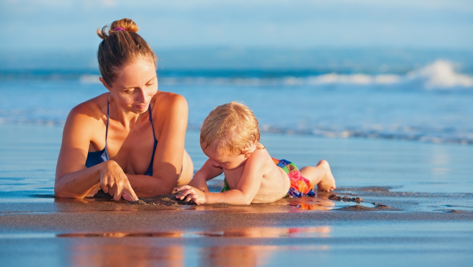 Happy family - mother, baby son play with fun on sea sand beach. Active parents and people outdoor activity on tropical summer vacations with children