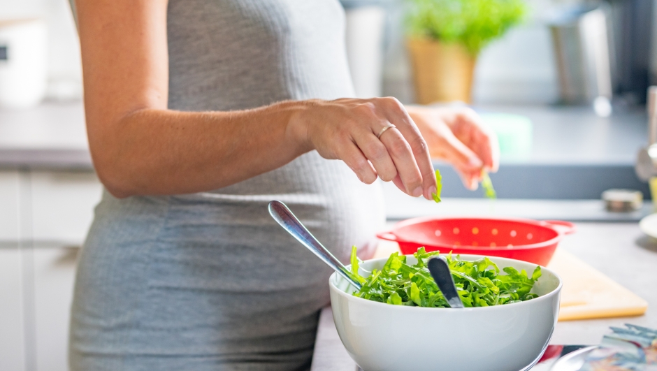 Pregnant woman's hands washing and selecting salad in the kitchen white salad bowl and red bowl in the back