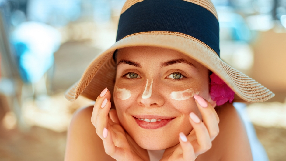 Skincare. Beauty Concept. Young pretty woman applying sun cream  and touch own face. Female in hat smear  sunscreen lotion on skin. Skin Protection and dermatology.