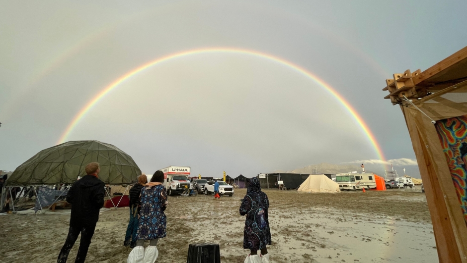 Attendees look at a double rainbow over flooding on a desert plain on September 1, 2023, after heavy rains turned the annual Burning Man festival site in Nevadas Black Rock desert into a mud pit. Tens of thousands of festivalgoers were stranded September 3, in deep mud in the Nevada desert after rain turned the annual Burning Man gathering into a quagmire, with police investigating one death. Video footage showed costume-wearing "burners" struggling across the wet gray-brown site, some using trash bags as makeshift boots, while many vehicles were stuck in the sludge. (Photo by Julie JAMMOT / AFP)