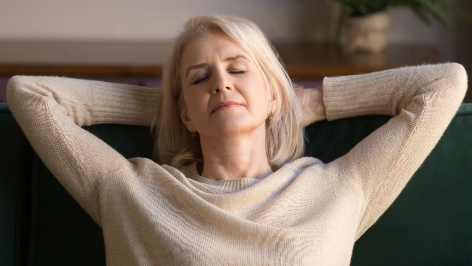 Calm middle aged woman relaxing enjoying weekend on comfortable sofa, grey haired carefree grandmother with hands behind head daydreaming, breathing, no stress peaceful free time at home close up