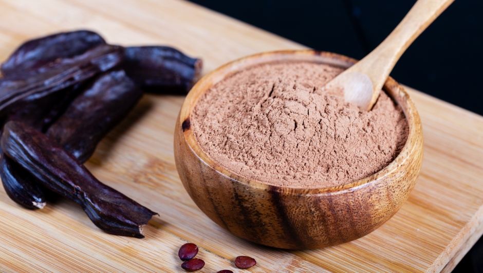 Carob pods and carob powder over wooden background