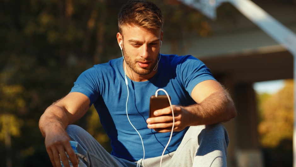 Handsome young man listening to music via smartphone and earbuds