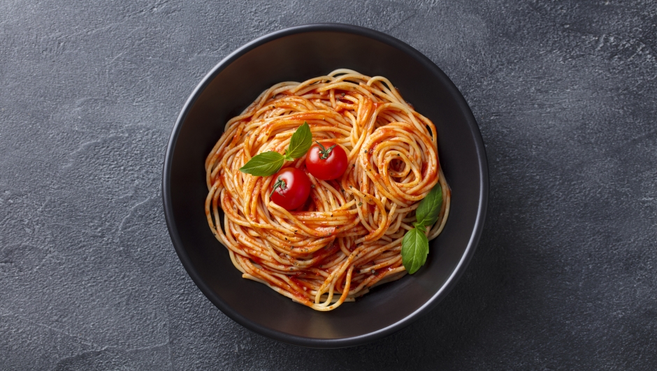 Pasta, spaghetti with tomato sauce in black bowl. Slate background. Top view