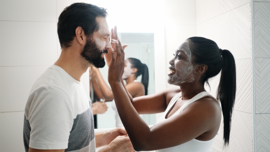 Multiethnic Couple Smiling and Laughing in Bathroom at Home. Happy Black Woman Applying Beauty Mask to Caucasian Man. Head and Shoulders