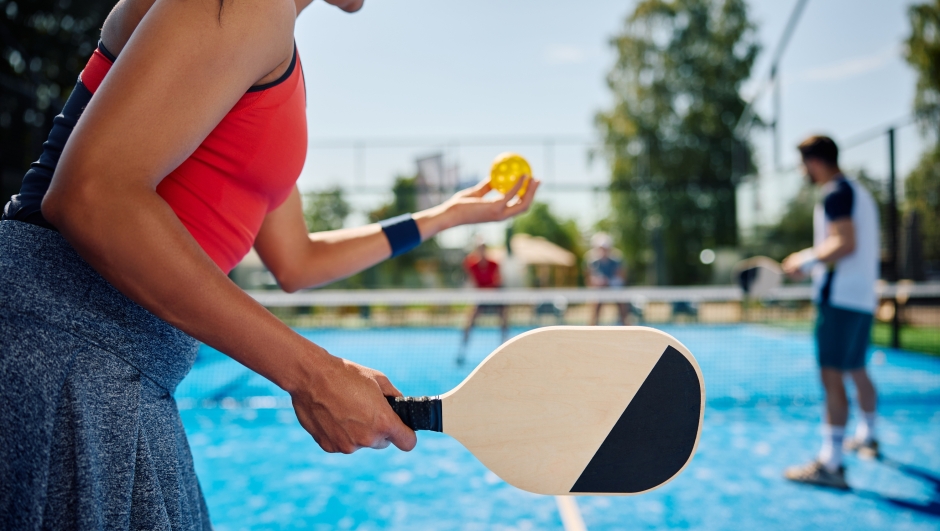 Unrecognizable African American woman serving the ball while playing mixed doubles in pickleball.