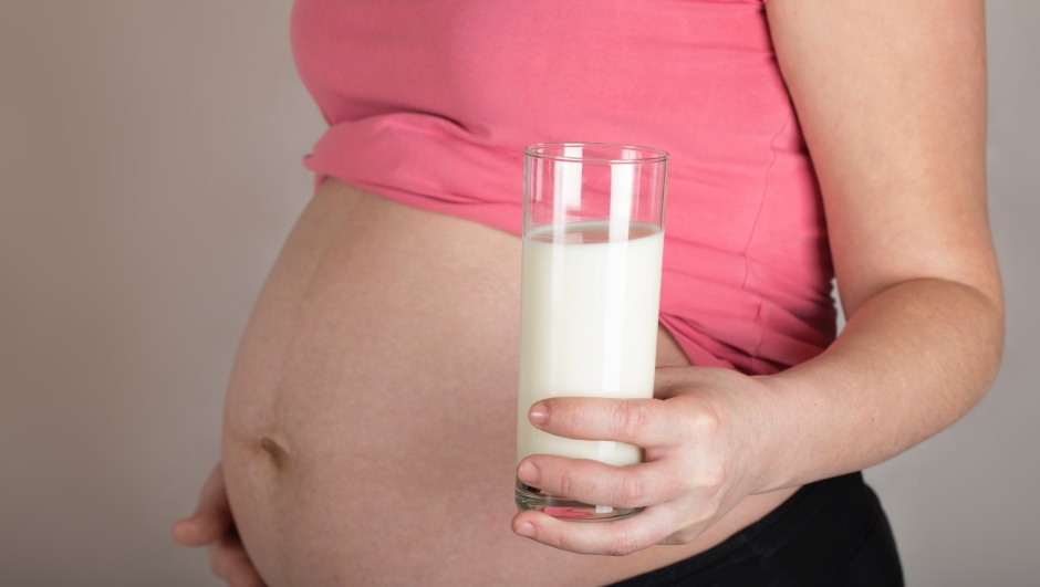 Young pregnant between 30 and 35 years old woman keeps a glass of milk. Closeup