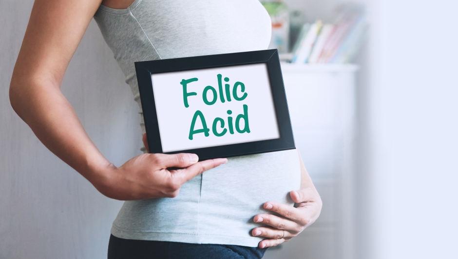 Pregnant woman holds whiteboard with text message - FOLIC ACID. Pregnancy, parenthood, preparation and expectation concept. Close-up, copy space, indoors.