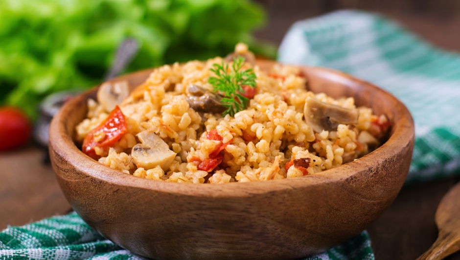 Bulgur with chicken, mushrooms and tomatoes in a wooden bowl. Top view