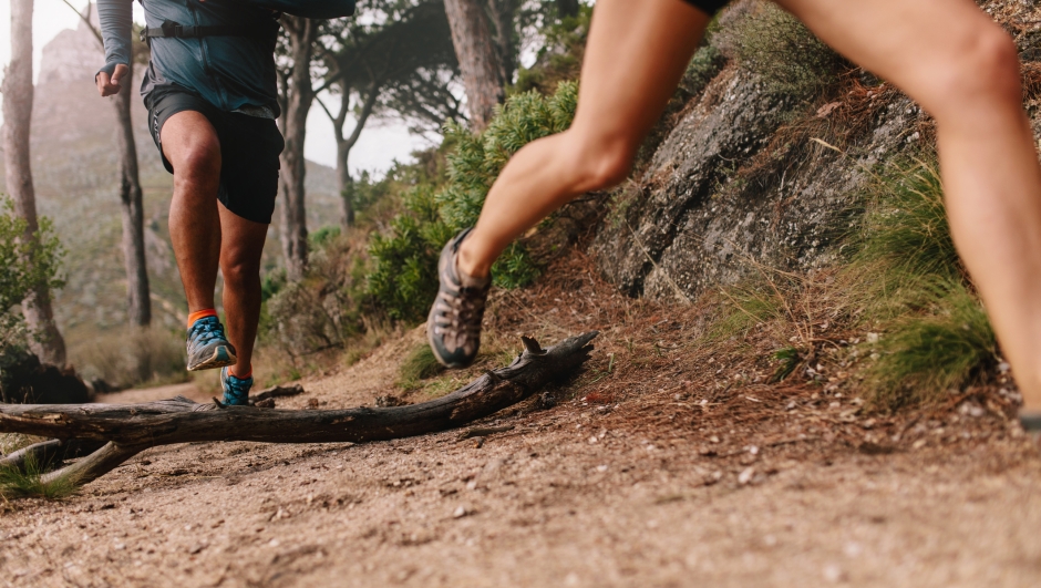 Healthy young couple running on mountain trail in morning. Young man and woman jogging on country path, focus on legs.