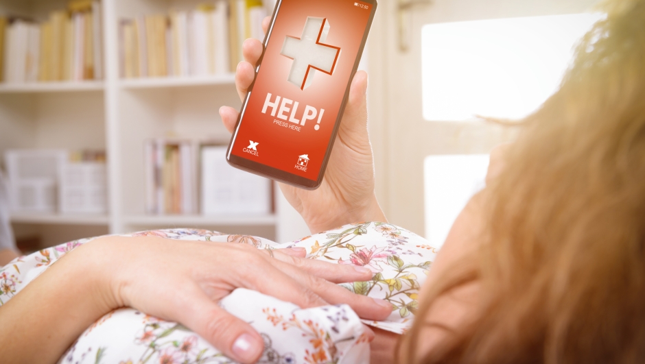 Woman holding her hand on the chest at home and using simple user-friendly smart phone application to call rescue team to prevent heart attack