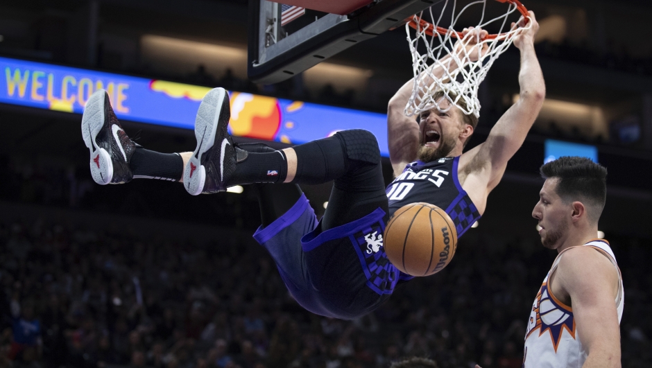 Sacramento Kings forward Domantas Sabonis hangs from the rim after a dunk next to Phoenix Suns forward Drew Eubanks during the second half of an NBA basketball game in Sacramento, Calif., Friday, Dec. 22, 2023. The Kings won 120-105. (AP Photo/José Luis Villegas)