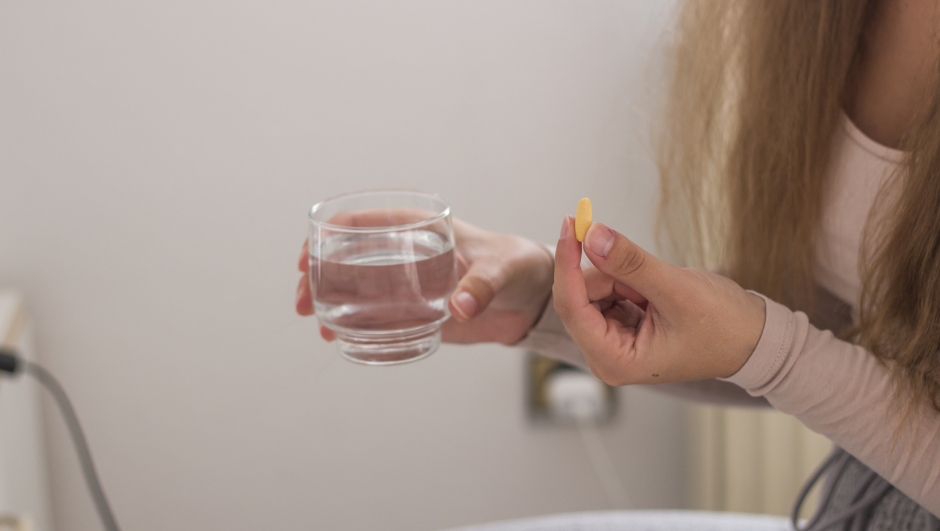 Close up cropped image of unrecognizable girl holding pill and glass of fresh water, taking medicine from head ache, stomach pain or taking vitamins, sedation meds, healthcare concept