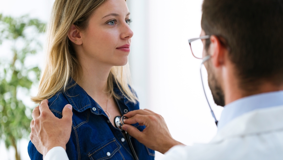 Shot of handsome young male doctor checking beautiful young woman patient heartbeat using stethoscope in medical office.