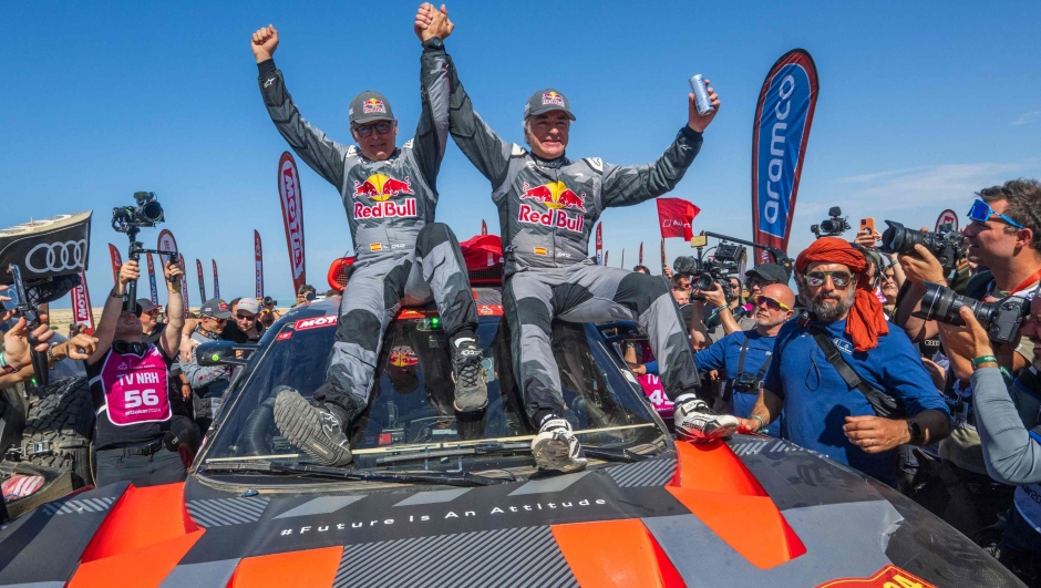 TOPSHOT - Team Audi Sport's Spanish driver Carlos Sainz (C,R) and his Spanish co-driver Lucas Cruz of (C,L) celebrate on their car after crossing the finish line of stage 12  of the Dakar rally 2024 from Yanbu to Yanbu, on January 19, 2024, at the end. Veteran Spanish driver Carlos Sainz won on January 19, 2024 the gruelling Dakar Rally for a fourth time on Friday, becoming at 61 the oldest winner of the race. (Photo by PATRICK HERTZOG / AFP)