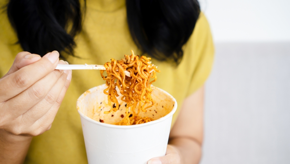 woman hand holding cup of spicy noodles, a woman eating noodle closeup