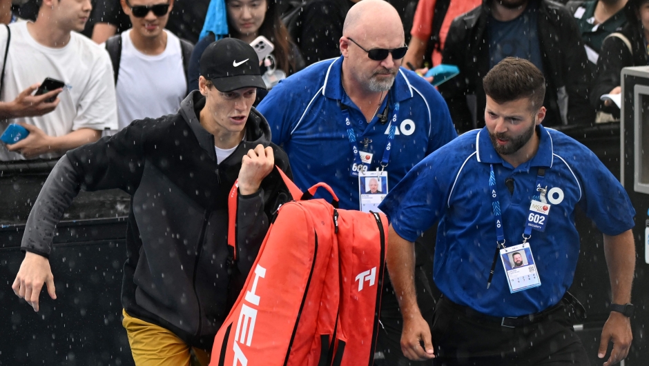 Italy's Jannik Sinner (L) leaves the court due to the rain during a training session on day 12 of the Australian Open tennis tournament in Melbourne on January 25, 2024. (Photo by Paul Crock / AFP) / -- IMAGE RESTRICTED TO EDITORIAL USE - STRICTLY NO COMMERCIAL USE --
