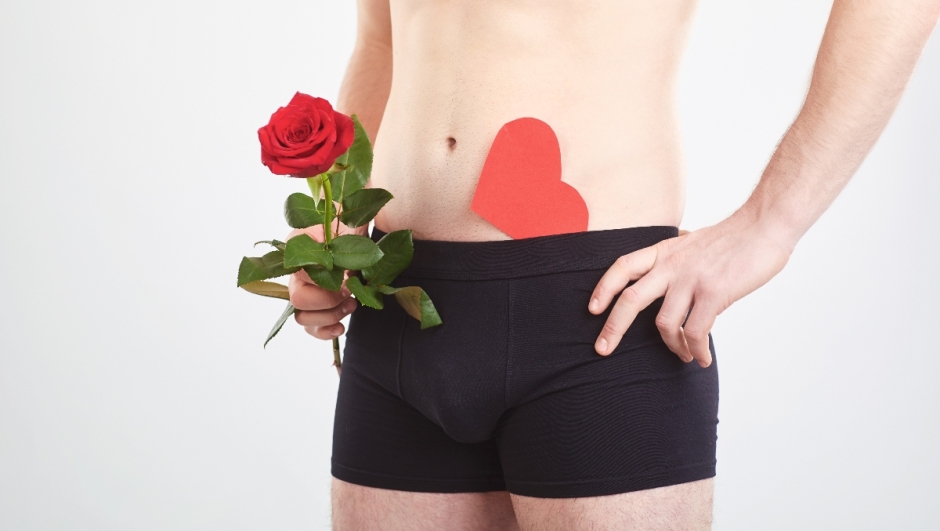 The concept of sex, lover. A man in black underwear holds rose and red heart in his hands.