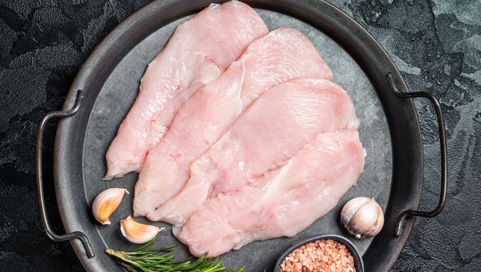 Raw sliced chicken breast fillet steaks in a steel tray, fowl meat. Black background. Top view.