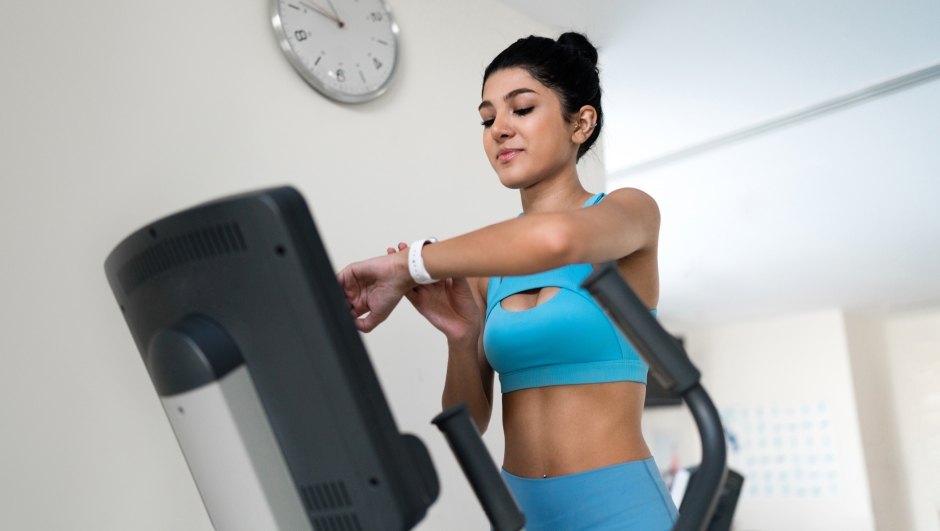 Young woman training at the gym using eliptical crosstrainer looking at her smart watch