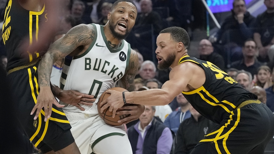 Milwaukee Bucks guard Damian Lillard (0) drives to the basket between Golden State Warriors forward Andrew Wiggins, left, and guard Stephen Curry during the first half of an NBA basketball game in San Francisco, Wednesday, March 6, 2024. (AP Photo/Jeff Chiu)