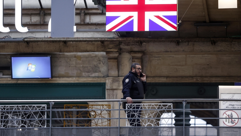 epa11049243 A French Customs Police officer stands near a Union Jack flag at Gare du Nord railway station in Paris, France, 30 December 2023. Flooding in southern England has caused numerous cancellations of Eurostar services from Paris and London St. Pancras railway stations. The French Railways service has announced fourteen trains were cancelled from Paris Gare du Nord due to weather conditions along Britainâ??s southern coast.  EPA/YOAN VALAT
