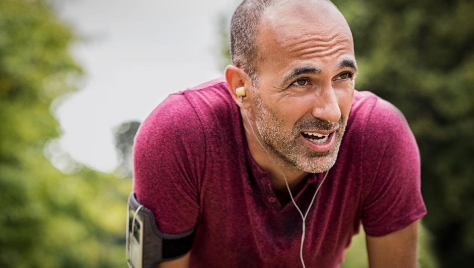 Portrait of athletic mature man after run. Handsome senior man resting after jog at the park on a sunny day. Sweaty multiethnic man listening to music while jogging.
