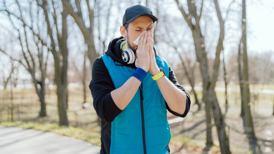 A man with a pollen allergy stands outside in a park. An athlete stops running practice due to a runny nose, blows his nose in a handkerchief. Illness interferes with exercise.