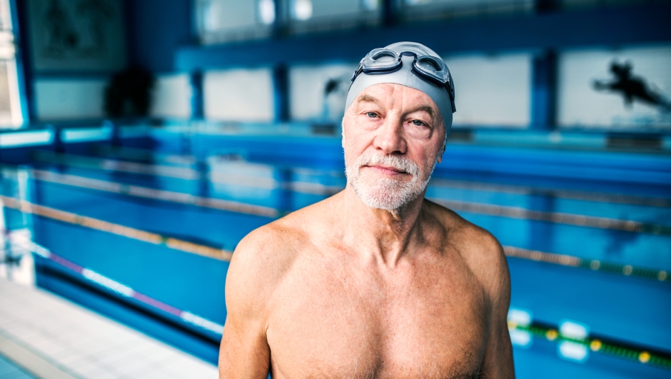 Senior man standing in an indoor swimming pool. Active pensioner enjoying sport.
