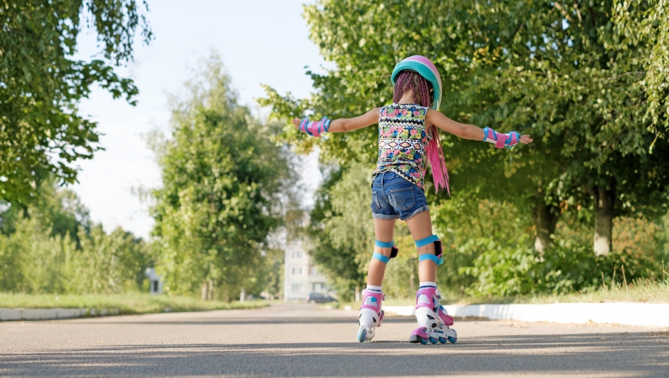 Kid tries to keep his balance and not fall, for the first time standing on roller skates. view behind. A girl is learning to rollerblade. Active sports for summer recreation and outdoor entertainment