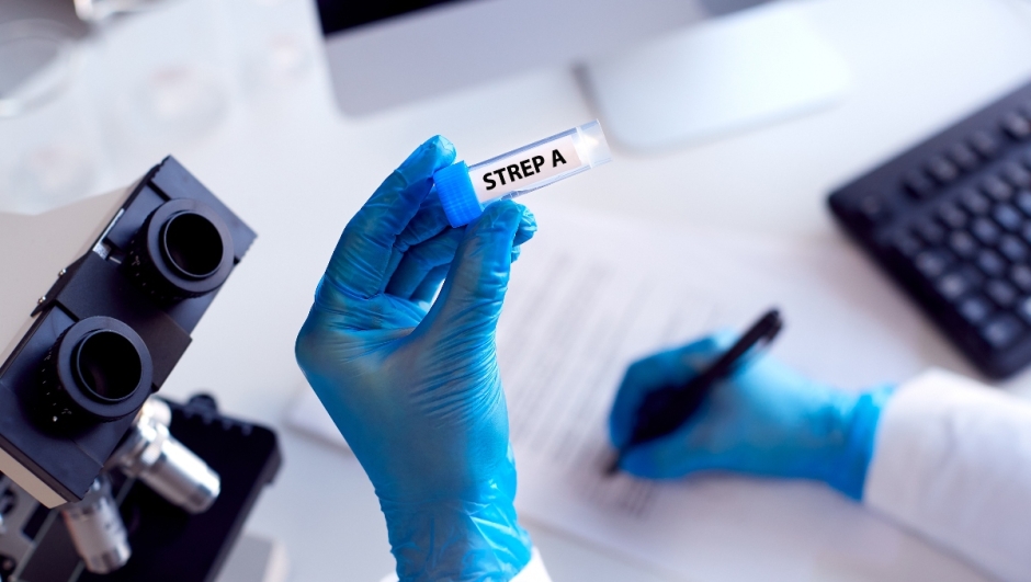 Close Up Of Lab Worker Conducting Research Using Microscope Holding Test Tube Labelled Strep A