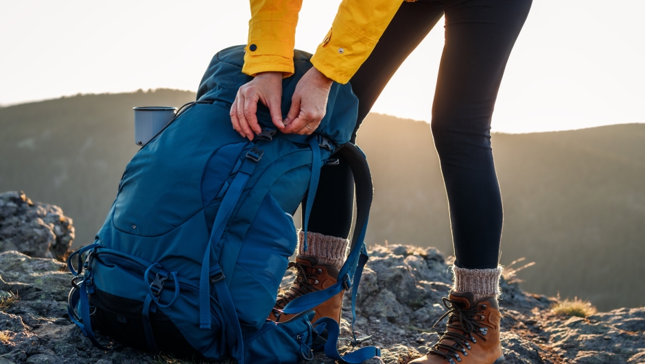 Woman opening backpack after climbing mountain peak. Hiking outdoors. Female tourist unpacking rucksack
