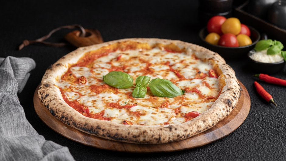 Pizza with basil, tomato, and cheese on wooden platter