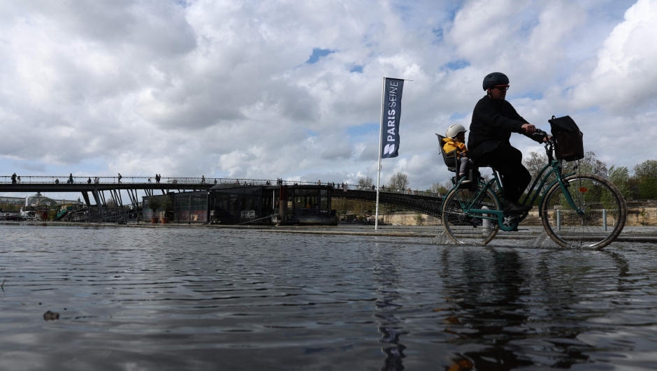 A man carries a child on a bicycle through the flooded docks along the Seine river, near the Passerelle Leopold-Sedar-Senghor bridge in Paris, on April 4, 2024. "On a national scale, the rainfall surplus was around 85 percent", compared with the 1991-2020 reference period, "i.e. the 5th wettest March since measurements began in 1958 (behind 2001, 1979, 1978 and 2006)", stated Meteo-France. (Photo by Emmanuel Dunand / AFP)