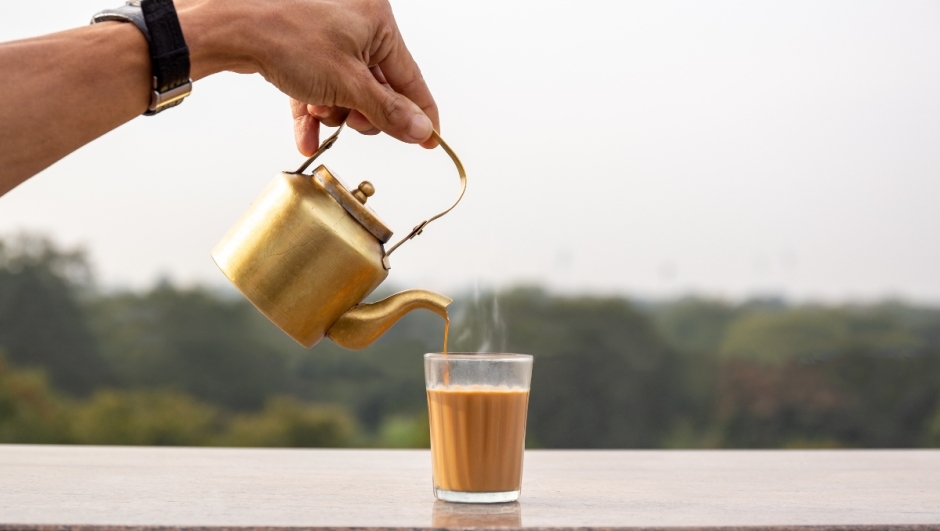 Hand pouring masala tea from a teapot into a glass