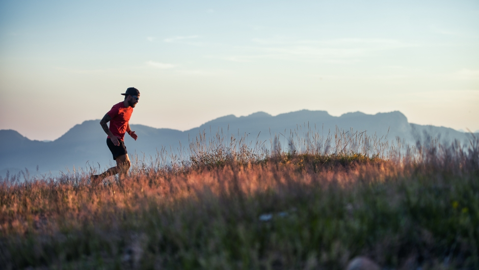 In a hilly sunset in colorful meadows a young sporty man runs alone