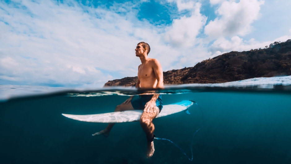 Surfer man with surfboard relaxing at line up in ocean