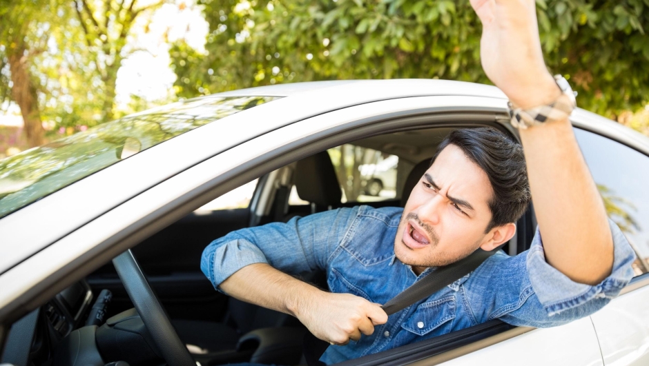 Portrait of angry young man sitting in his car shouting and gesturing at other drivers during traffic on road