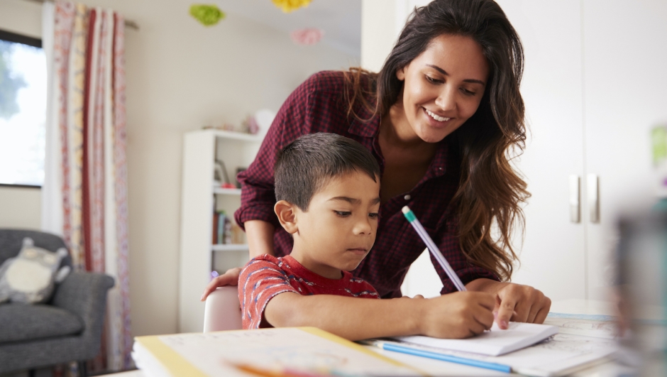 Mother Helping Son With Homework Sitting At Desk In Bedroom