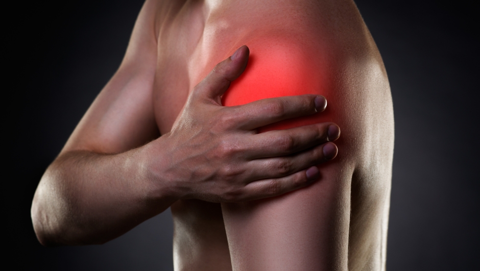 Man with pain in shoulder on black background, studio shot with red dot