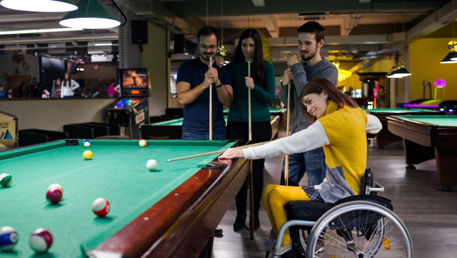 Disabled girl in a wheelchair playing billiards with friends