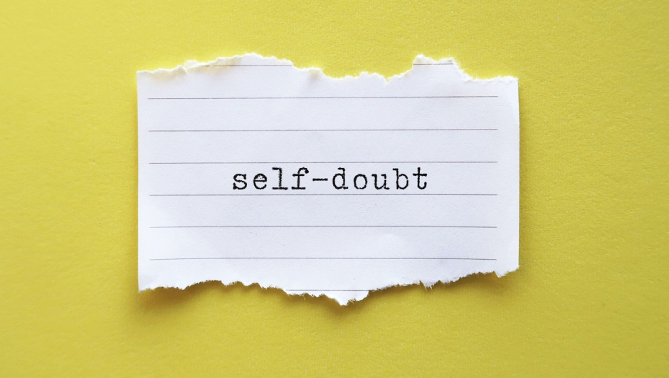 Torn ote on yellow background with text  Self-doubt - means lacking of confidence or have a mindset that holds you back from succeeding leads to imposter syndrome or self-sabotage