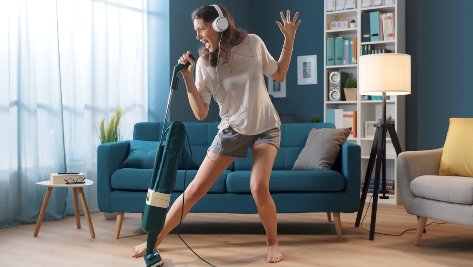 Cheerful woman cleaning up her home and singing, she is using the vacuum cleaner as a microphone