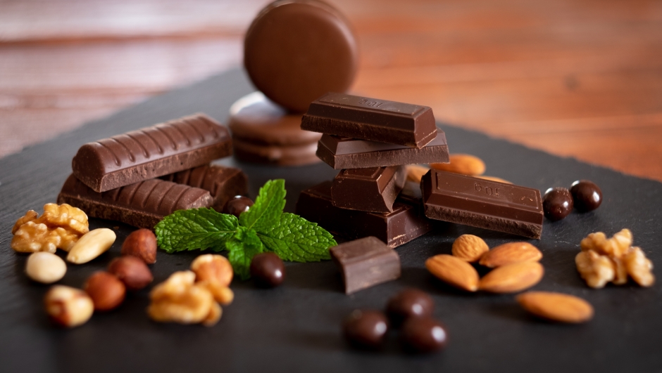 Pieces of dark chocolate and dried fruit on black background. Wooden table and back lit